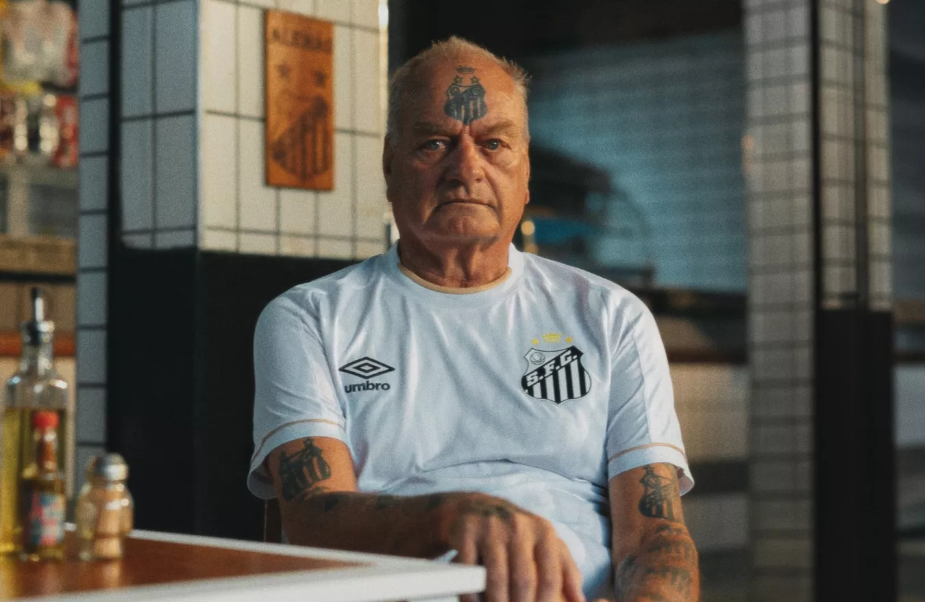 Homem idoso com a camisa branca do Santos sentado em um bar