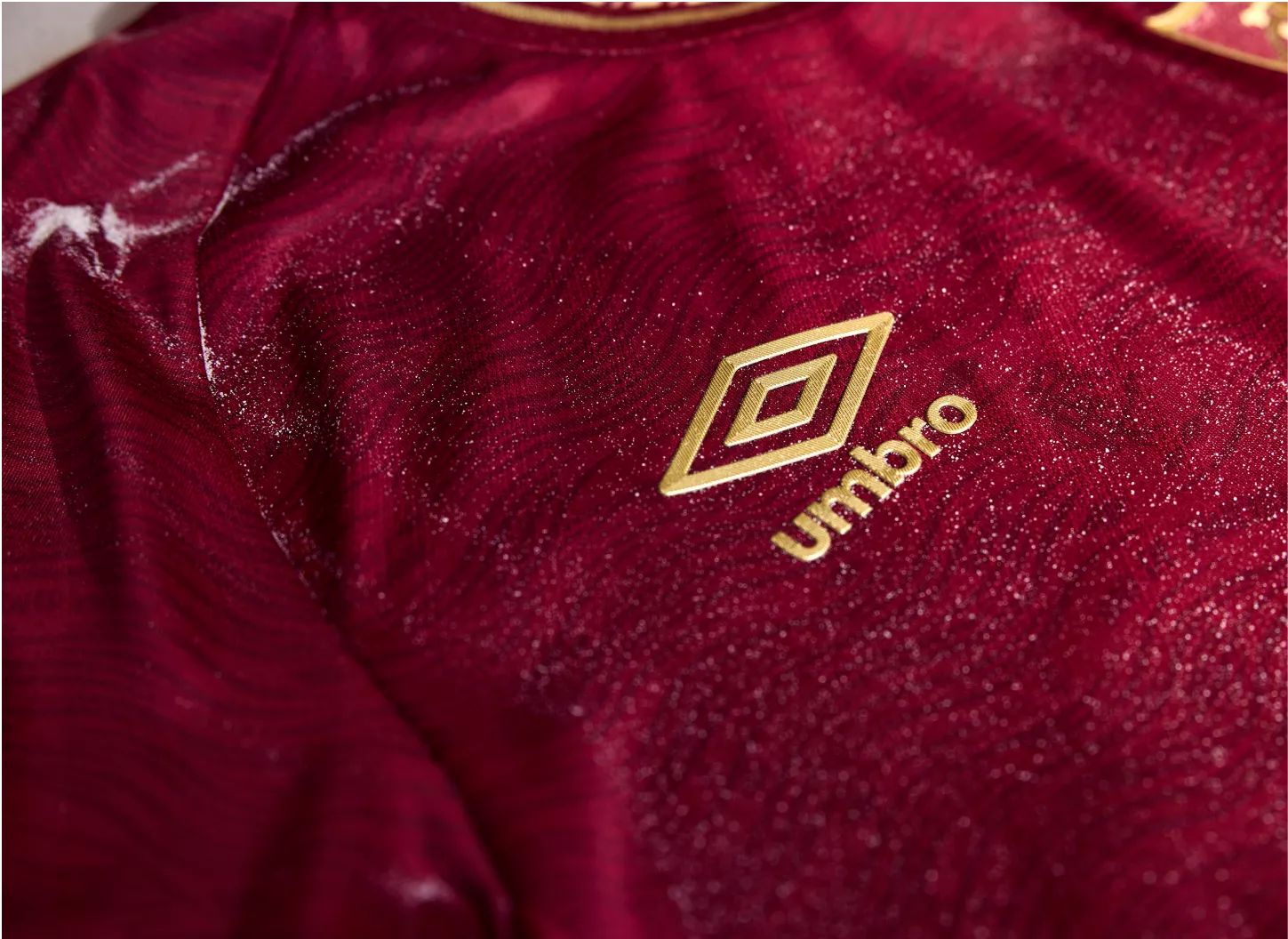 Detalhe do logo Umbro dourado na camisa grená do Fluminense